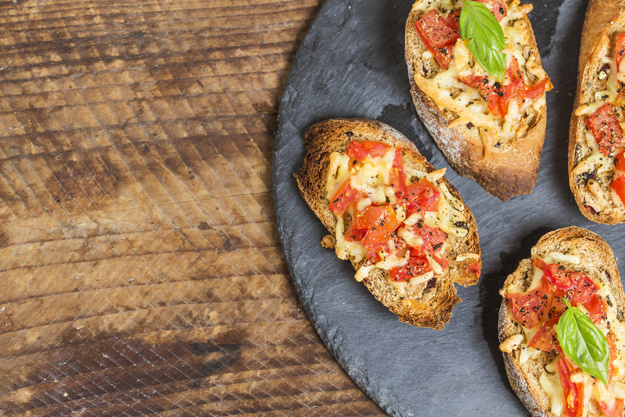 Italian bruschetta with roasted tomatoes, mozzarella cheese and herbs on a cutting board